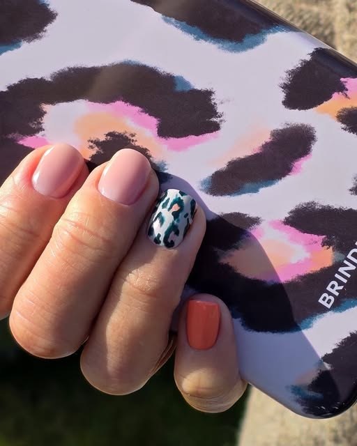 Neutral pink nails with a teal leopard-print accent nail and a coral nail, against a leopard-print phone case